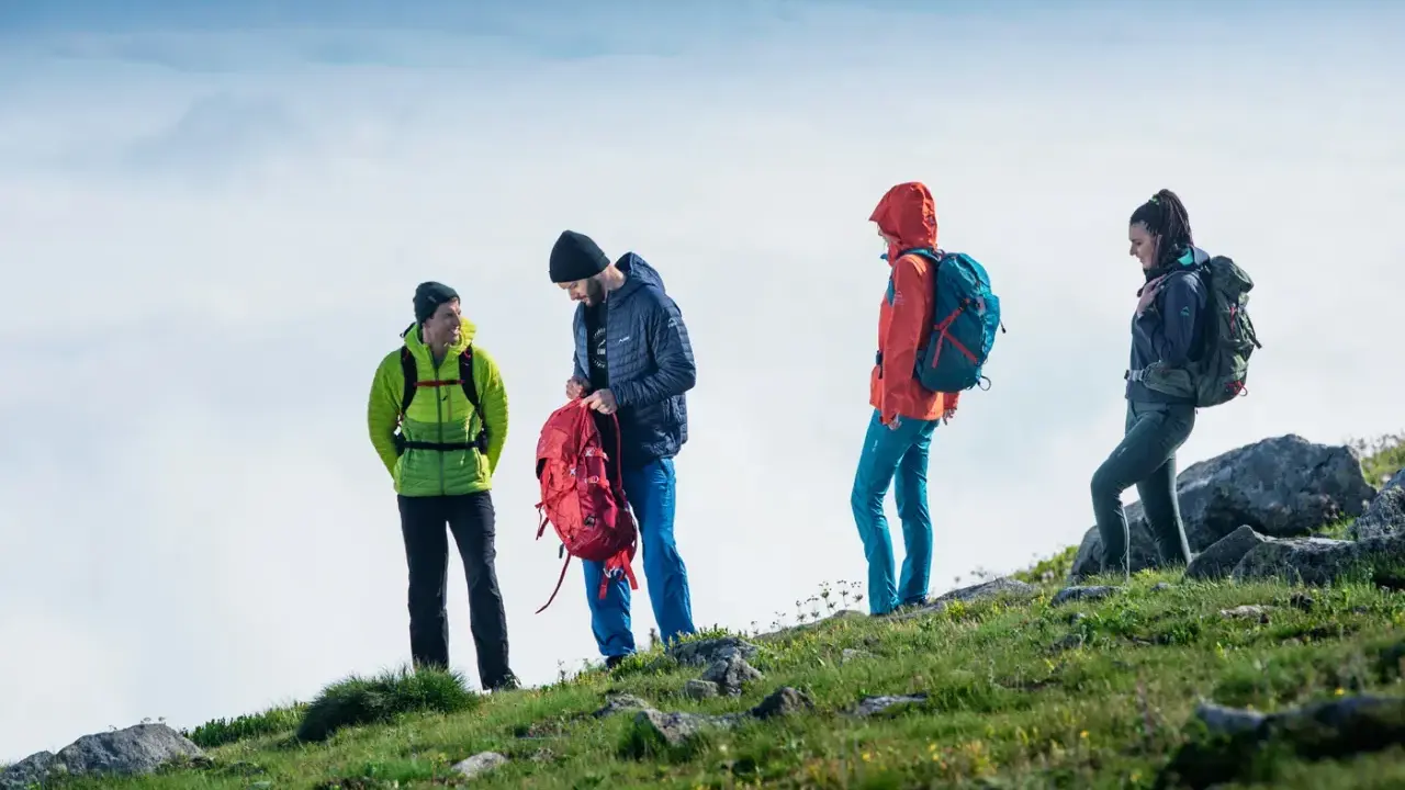 Czterech turystów w górskim krajobrazie, przygotowujących się do wyprawy. To właśnie jest co to trekking – przygoda i odkrywanie.