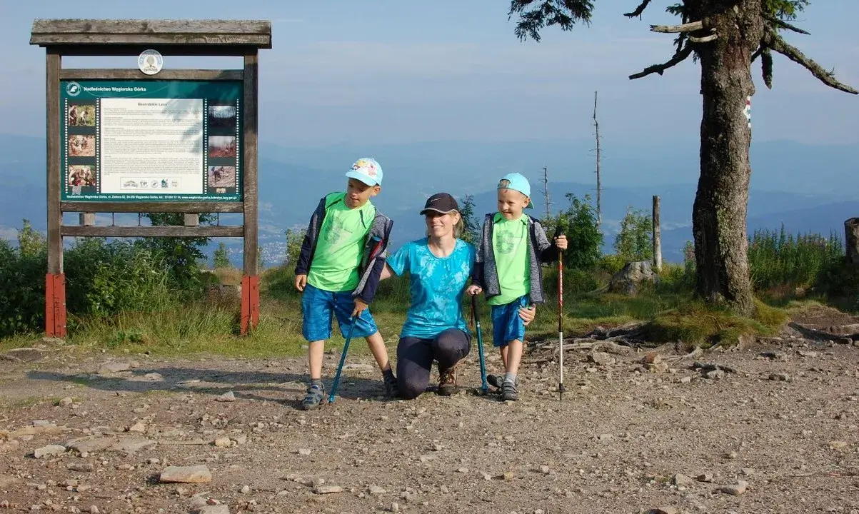 Rodzina na szczycie Baraniej Góry. Dzieci z kijkami trekkingowymi, mama klęczy obok.