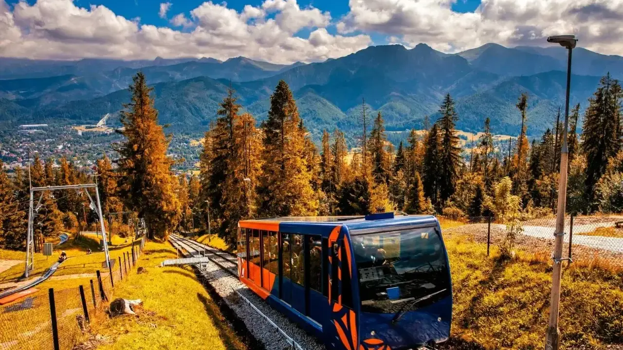 Kolejka linowo-terenowa na Gubałówkę, z widokiem na Tatry. Jesienne kolory drzew i błękitne niebo. Wejście pieszo na Gubałówkę to wspaniała przygoda.