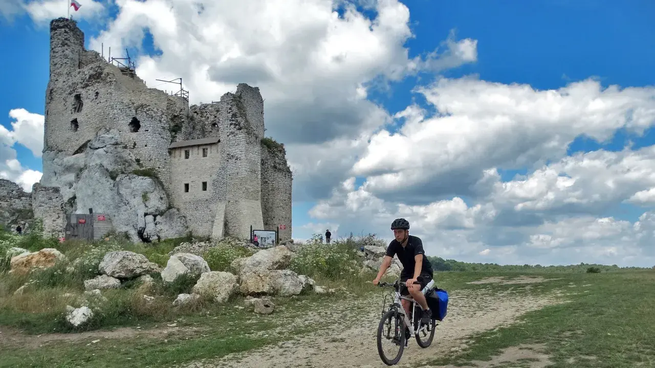 Rowerzysta na szlaku jura krakowsko częstochowska trasa, obok ruin zamku na skale.