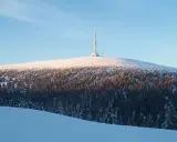 Wieża na ośnieżonym szczycie góry, otoczona lasem iglastym.