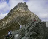 Widok na skalistą przełęcz pod chłopkiem. W oddali widać szlak, a na pierwszym planie siedzi turysta.