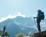Kobieta z plecakiem i kijkami trekkingowymi podziwia majestatyczne góry podczas trekkingu do Everest Base Camp.