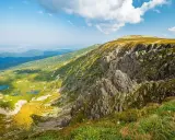 Widok na skaliste zbocze Szrenicy i malownicze Śnieżne Kotły z górskimi stawami w dole.