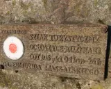 Tabliczka na skale z czerwono-białym kołem i napisem "Główny szlak świętokrzyski im. Edmunda Massalskiego".
