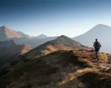 Wędrowiec na grani Tatr, idealne tatry szlaki dla średnio zaawansowanych. Słońce oświetla trawiaste zbocza i skaliste szczyty.