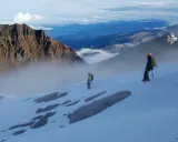 Dwóch alpinistów na ośnieżonym zboczu, w tle majestatyczne góry Ekwadoru, w tym najwyższy szczyt ekwadoru.