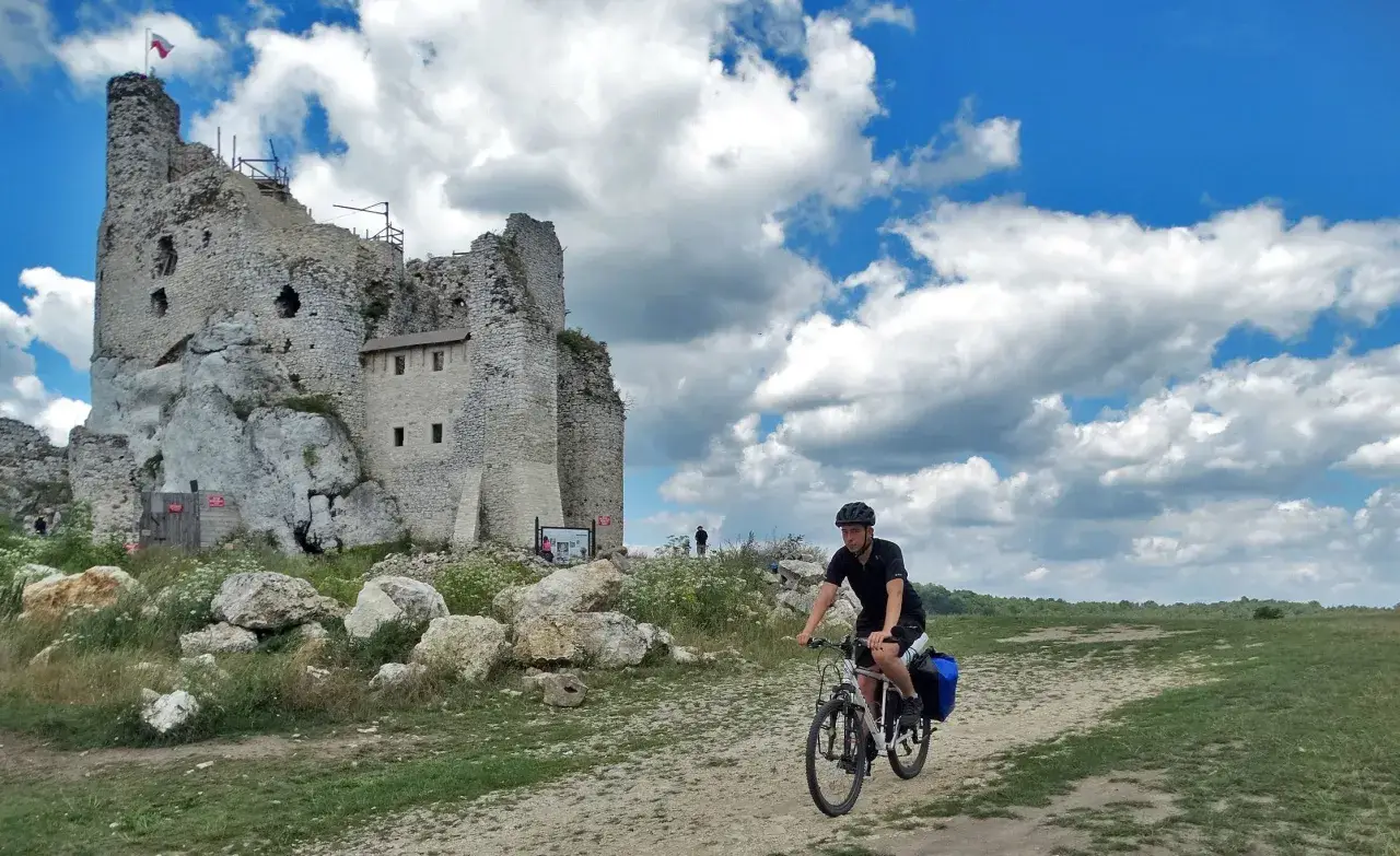 Rowerzysta na szlaku jura krakowsko częstochowska trasa, obok ruin zamku na skale.