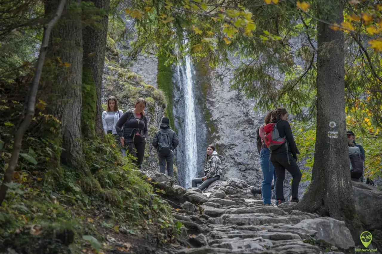 Grupa turystów na kamienistej trasie przy wodospadzie Siklawica. Wodospad Siklawica to cel wędrówki.