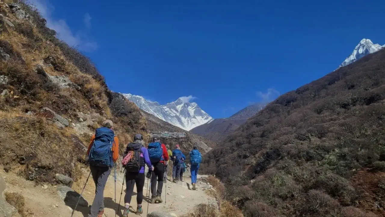 Grupa turystów wyrusza na trekking w Himalajach. W oddali widać ośnieżone szczyty i wioskę.