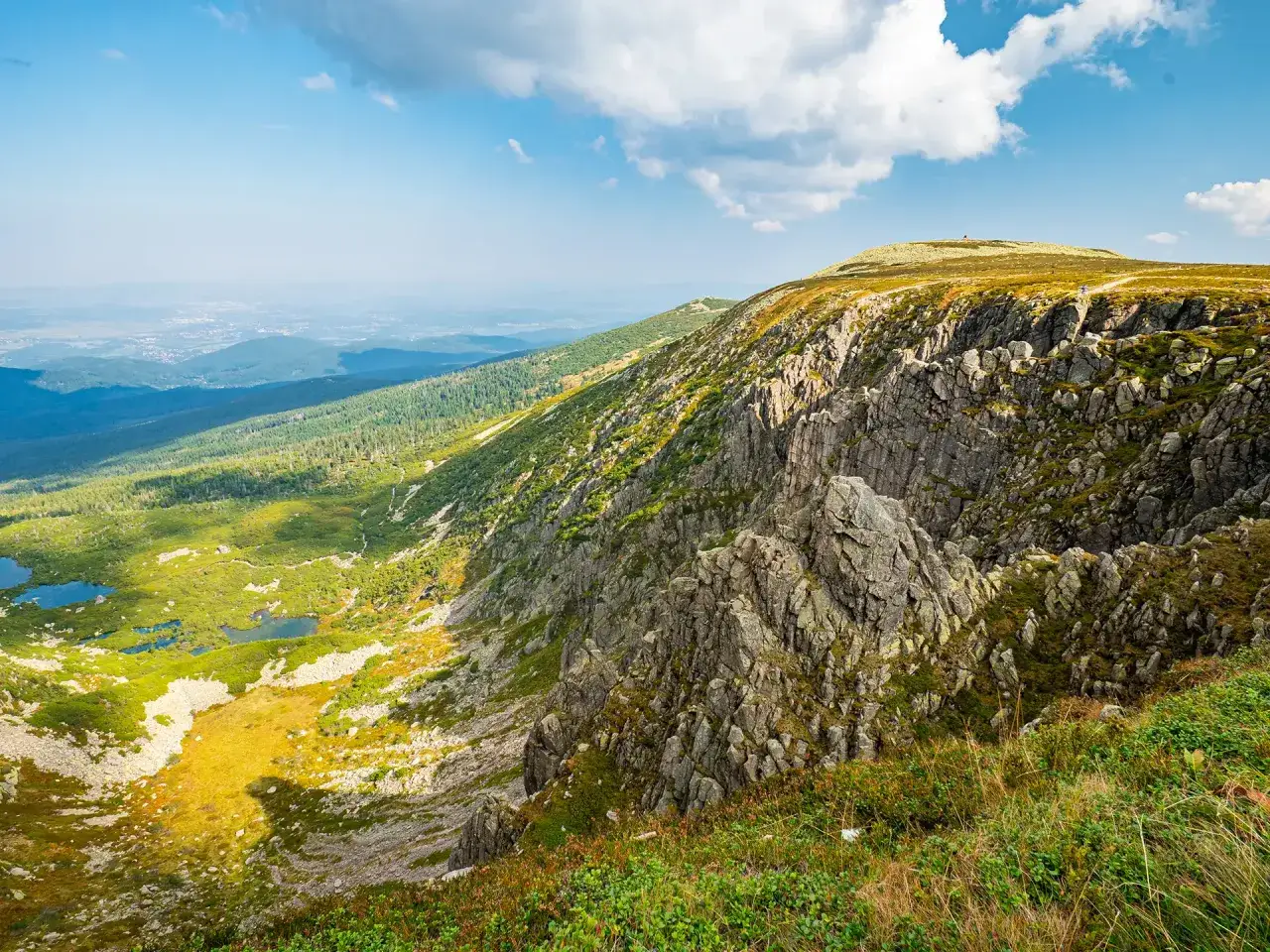 Widok z trasy na Śnieżne Kotły: skaliste zbocza, zielone doliny z jeziorkami i daleka panorama.