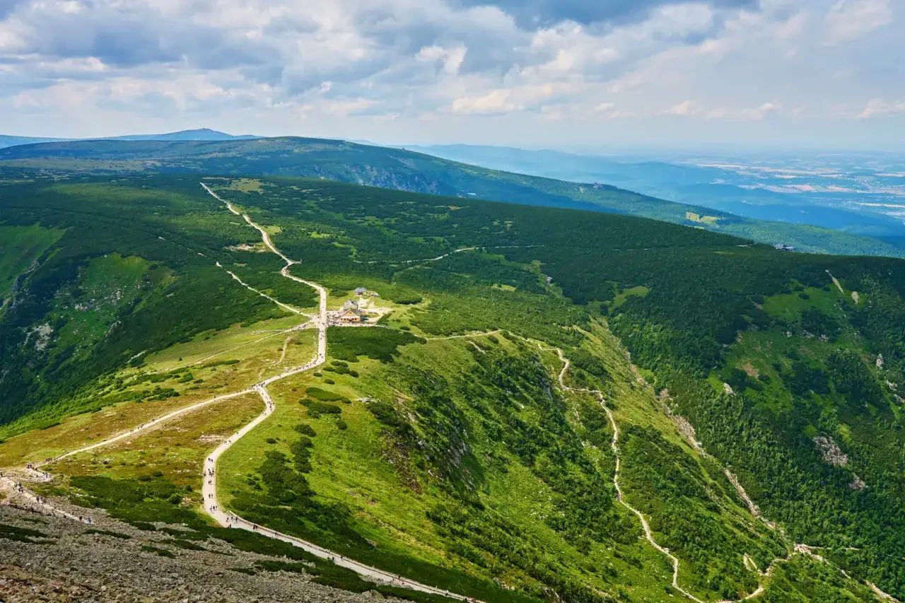 Schronisko Odrodzenie w Karkonoszach, otoczone zielonymi zboczami i wijącymi się szlakami, gdzie turyści podziwiają panoramę.