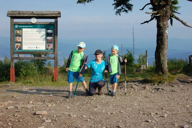 Rodzina na szczycie Baraniej Góry. Dzieci z kijkami trekkingowymi, mama klęczy obok.